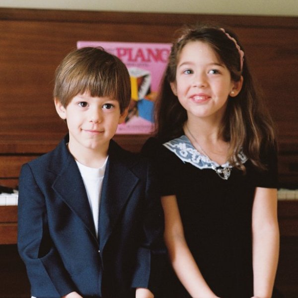 boy and girl standing in front of piano